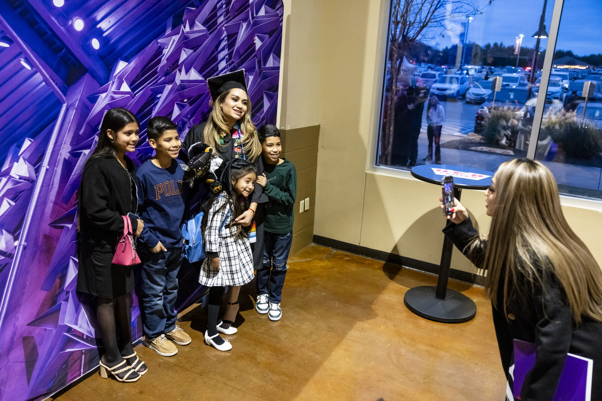 A woman takes a picture of an ACC graduate with her children, capturing their happiness and the moment they are sharing together.