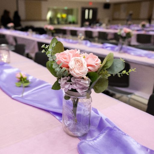 A vase of pink roses, a pale purple ribbon, and a pink tablecloth adorn a table at the banquet of the ACC Women’s Health, Motivation, and Empowerment Conference