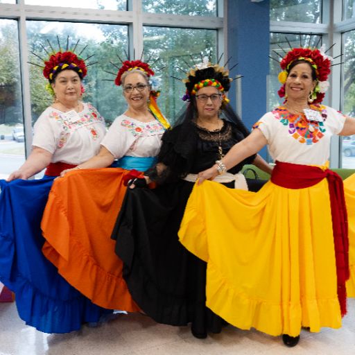 Four dancers in traditional brightly colored skirts and headdresses pose for a picture at the ACC Women’s Health, Motivation, and Empowerment Conference