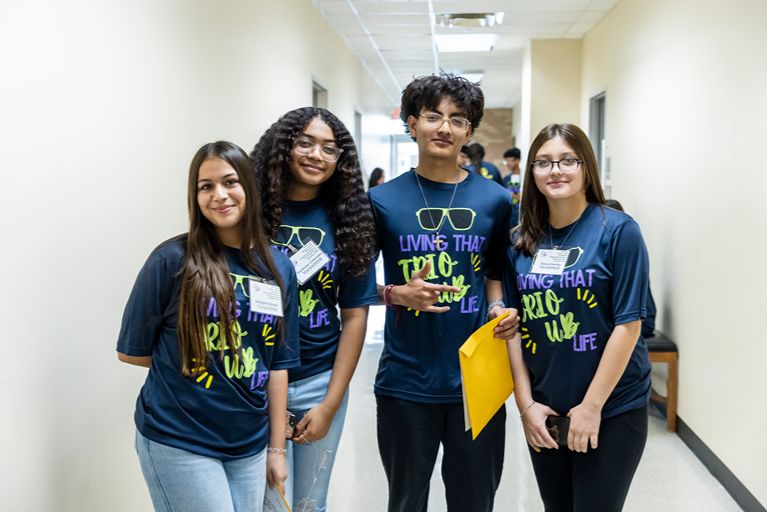 four students wearing living that trio club life t shirts pose in a hallway.